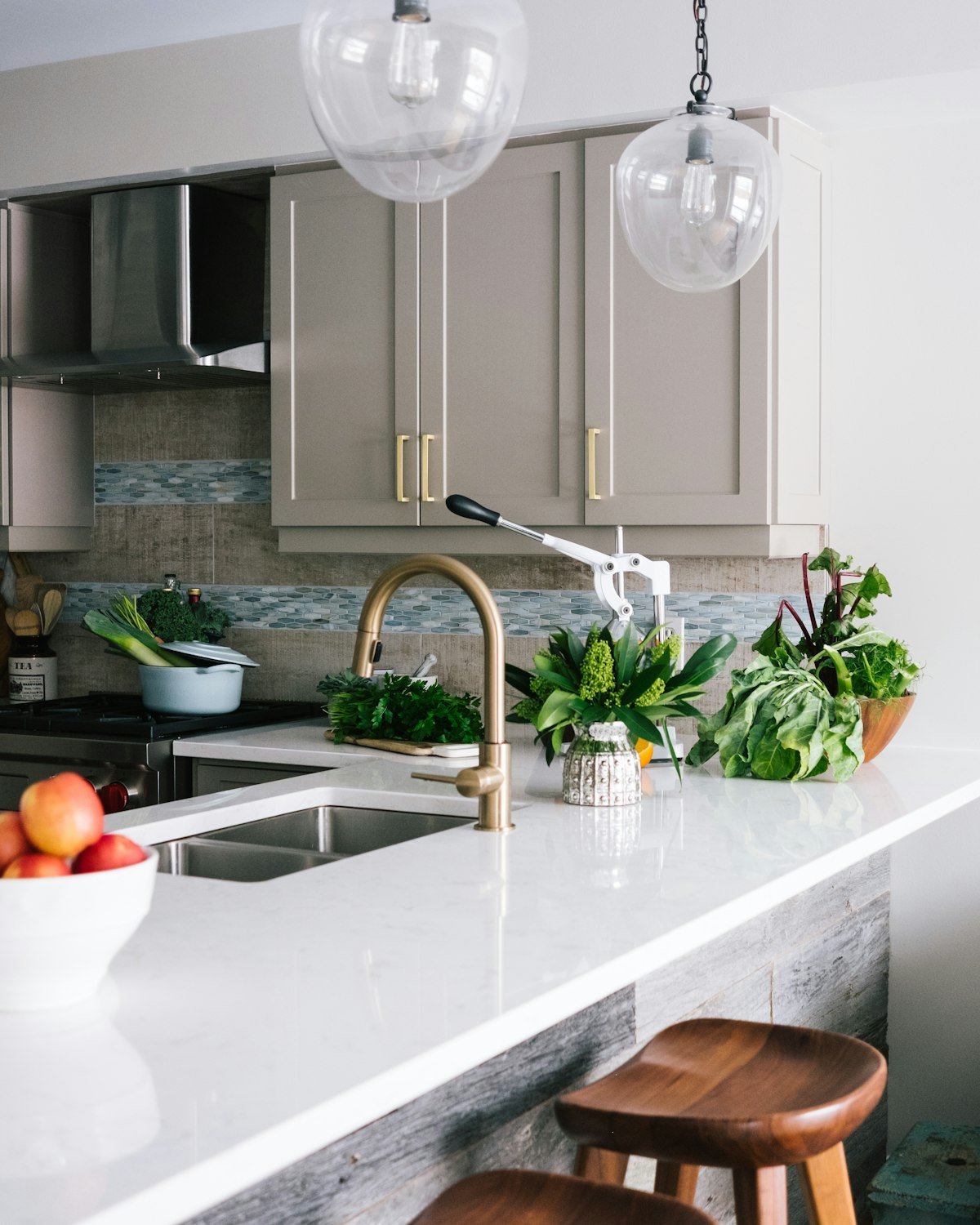 Quartz waterfall island with a brushed brass faucet, gray cabinets and pendant lighting